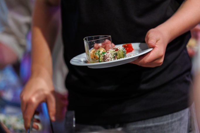 Eine Person hält einen Teller mit verschiedenen Salaten und einer kleinen Schale.